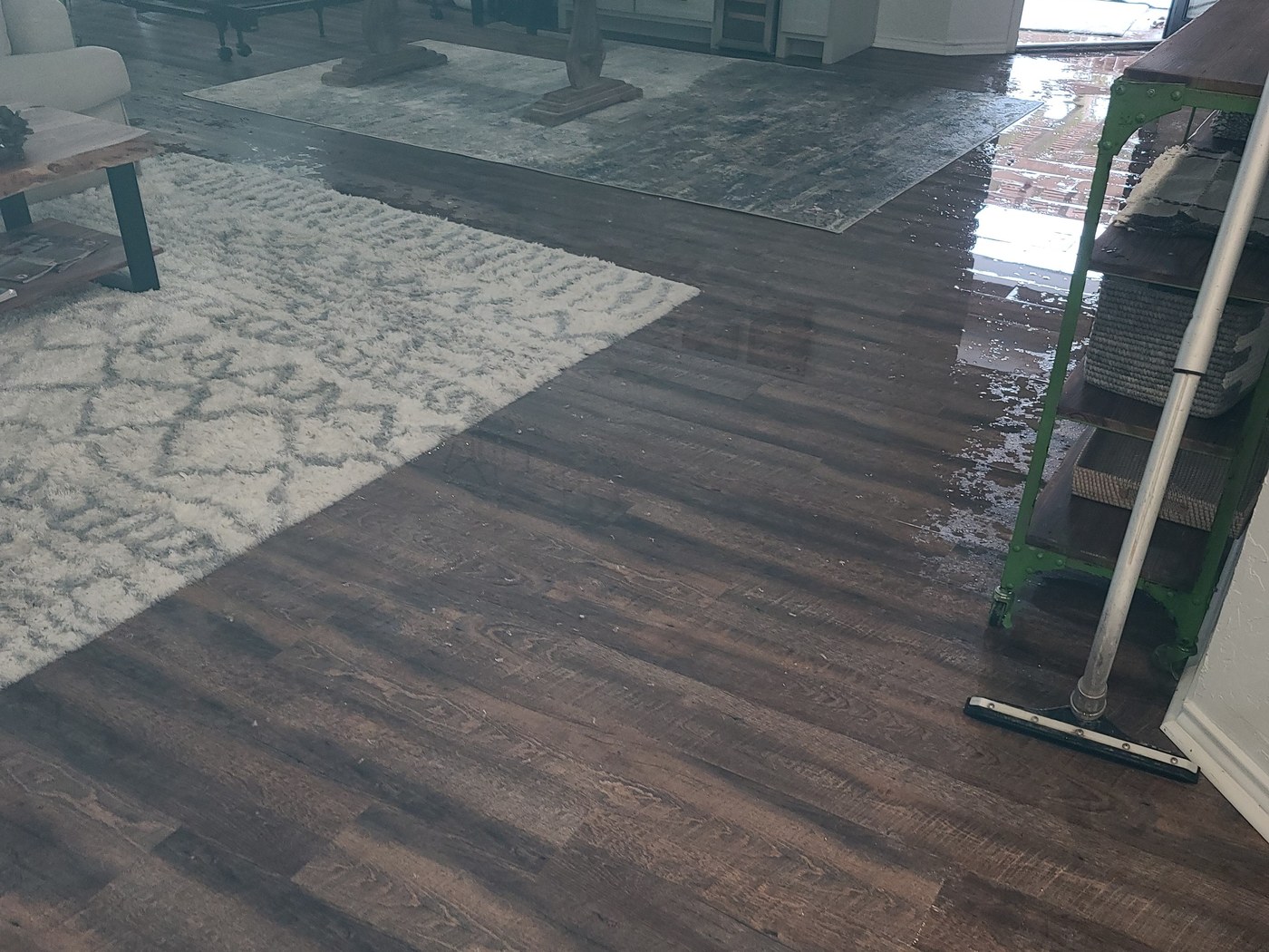 Standing water covering a hardwood living room floor after a flood, with a squeegee and equipment staged for extraction
